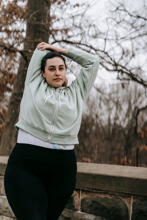 Free Young overweight focused female looking away and warming up in autumn park with leafless trees in daytime Stock Photo