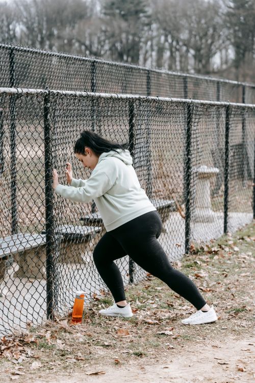 Free Side view of determined plus size female athlete in sportswear leaning on chain link fence while training in city park on cloudy autumn day Stock Photo