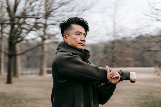 Young Asian man stretching arms outdoors in an autumn park, focusing on fitness and wellness.