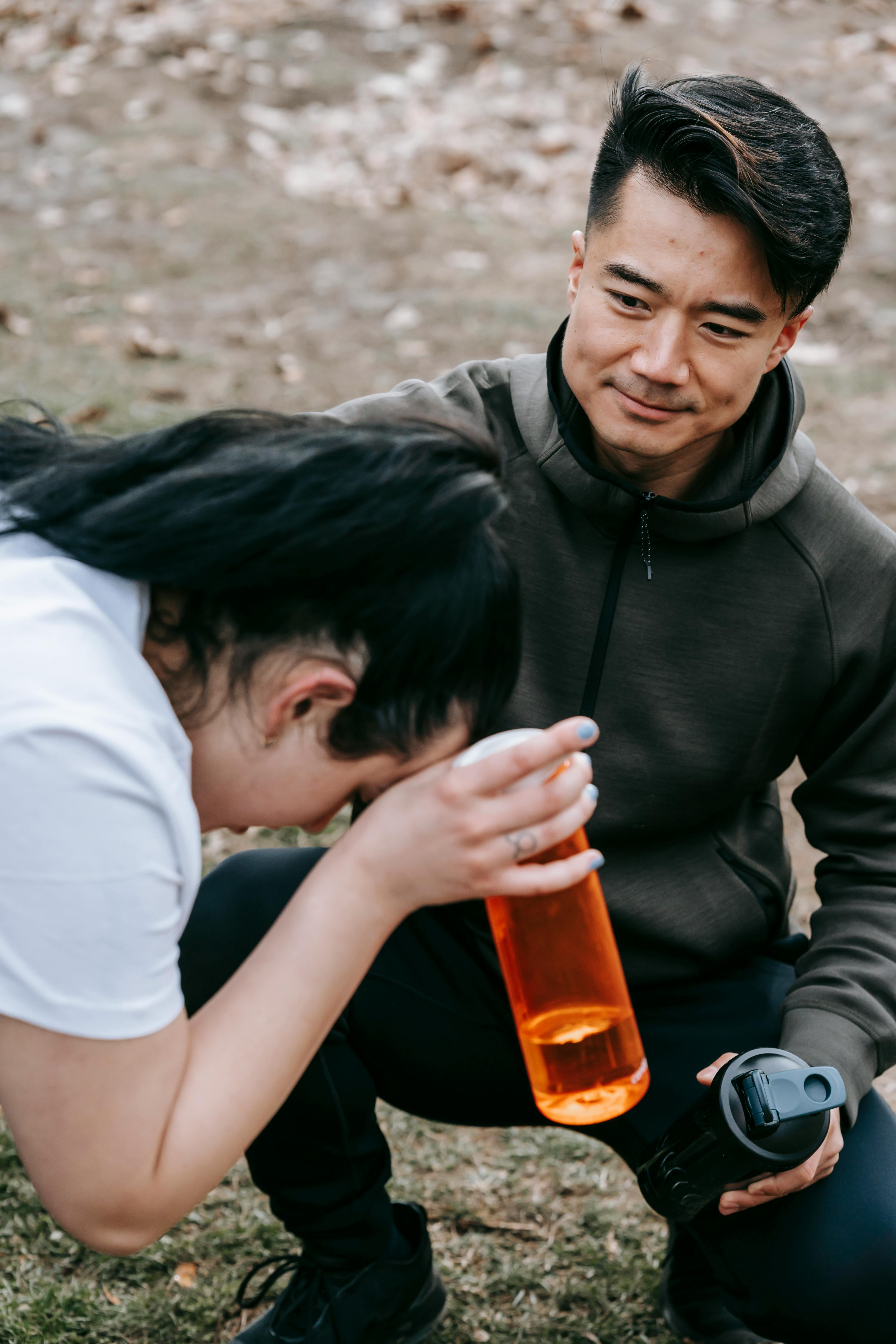 young asian trainer supporting young overweight woman with bottle