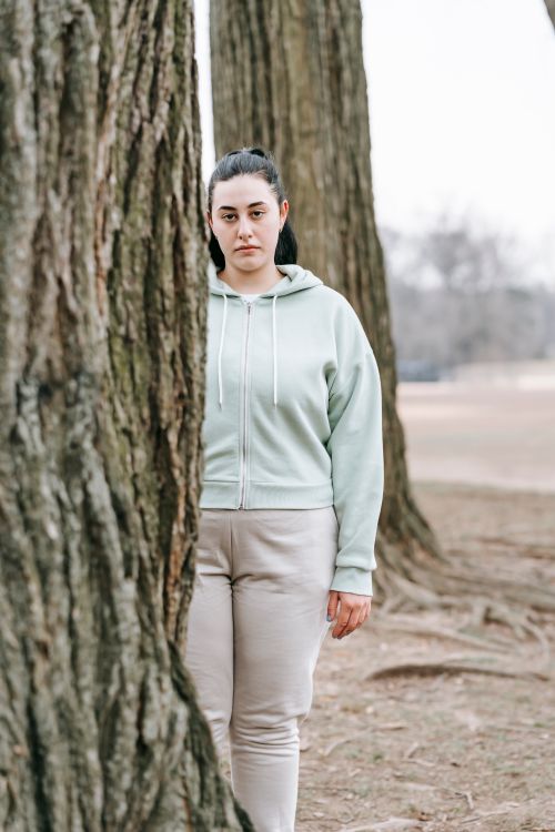 Free Pensive plus sized female in casual clothes standing behind tree placed in park and looking at looking at camera Stock Photo
