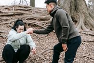 Ethnic man in sportswear helping overweight female with dark hair get up from ground in park in daytime