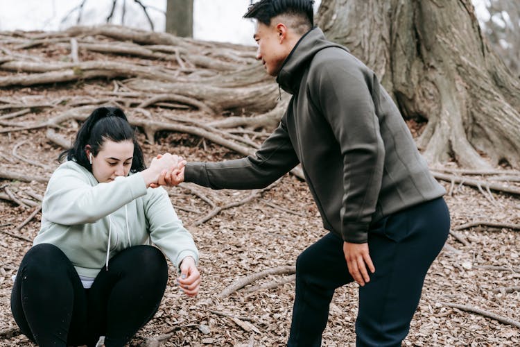 Man Helping Plus Sized Woman Get Up From Ground In Park