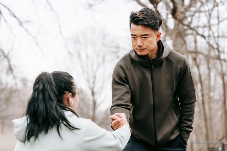 Serious Asian Man Giving Hand To Woman In Park In Daytime