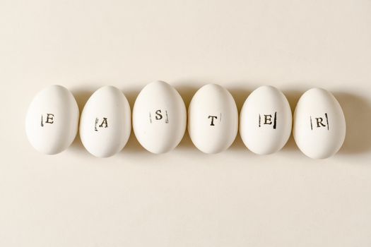 Close-up of white Easter eggs with stamped letters, arranged in a minimalist style on a white surface.
