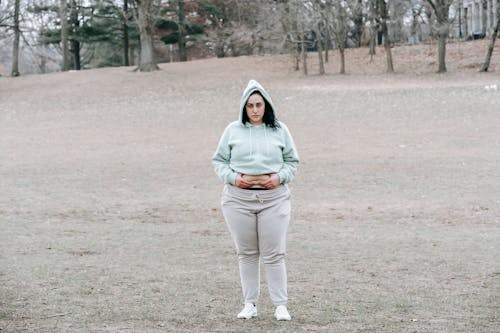 Free Full length of unhappy young woman in activewear standing in autumn park and showing fat on waist Stock Photo