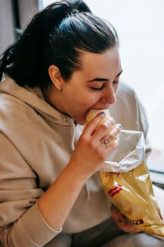 Woman enjoying a bag of potato chips indoors, indulging in a tasty snack craving.