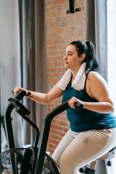 Side view of young overweight female in fitness outfit doing exercises on cycle in gym