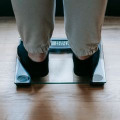 Standing on a glass bathroom scale with a digital display on a wooden floor