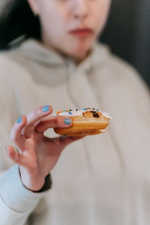 Free Crop unrecognizable pensive female looking at delicious doughnut with doubts while chewing forbidden dessert Stock Photo