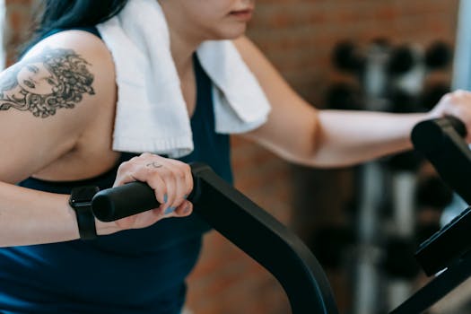 Woman with tattoo working out on exercise bike indoors, showing determination.