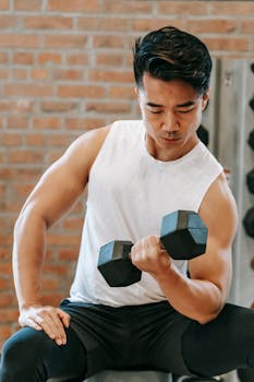 Asian man lifting a dumbbell indoors, showcasing focus and fitness.