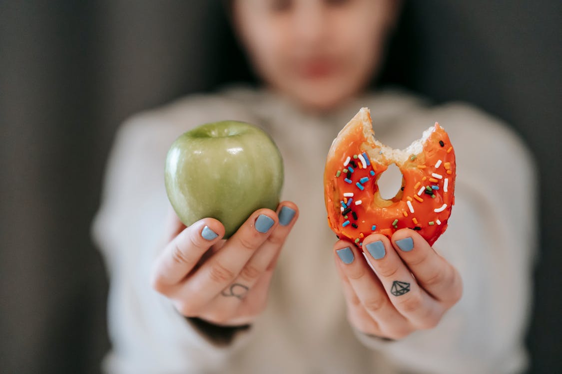 woman trying to resist sugar holding up apple and donut
