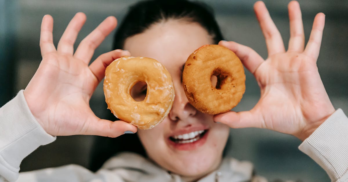 Positive young female in casual clothes smiling while covering eyes with delicious doughnuts