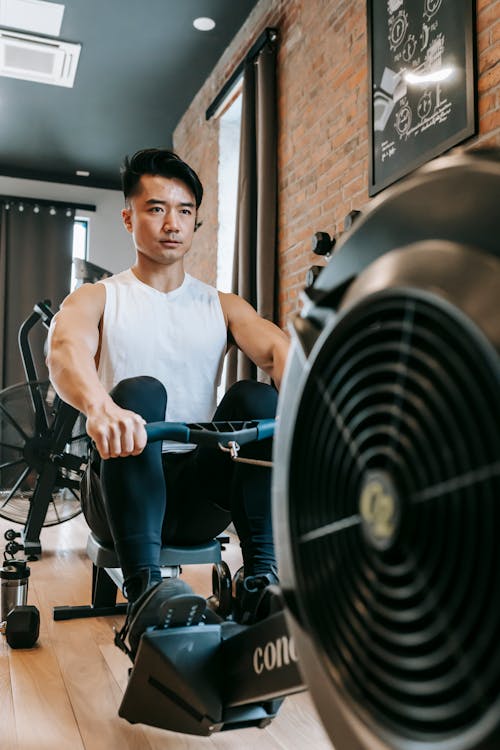 Full body of focused muscular male athlete in sportswear sitting and looking forward while training on exercise equipment