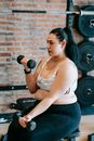Side view of overweight female in activewear doing exercise with dumbbells during weight loss workout in sports club