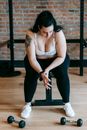 Full body of obese tired female in activewear having break in training with dumbbells in gym