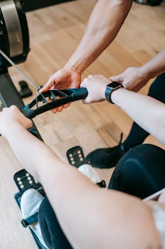 Close-up of a personal trainer guiding a client on a rowing machine during a workout session.