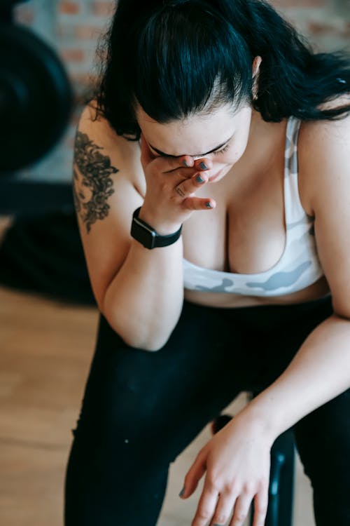 High angle of upset overweight female in sportswear wiping tears while crying in sports club