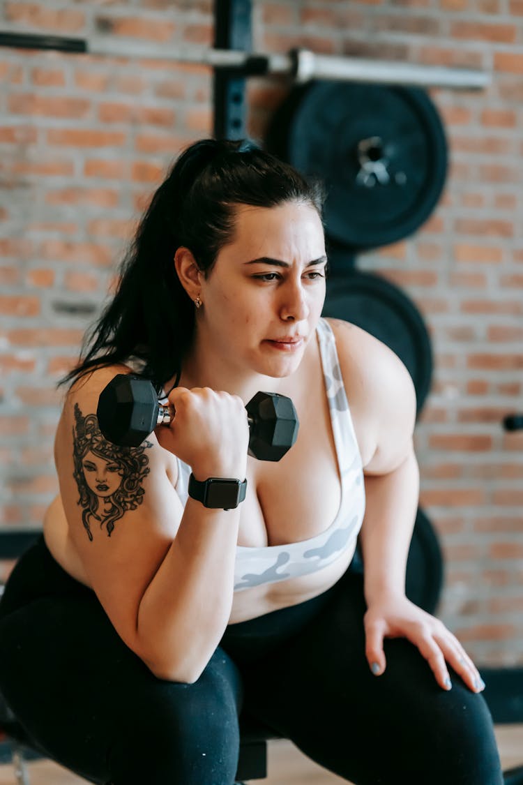 Focused Overweight Female Lifting Dumbbell In Training Studio