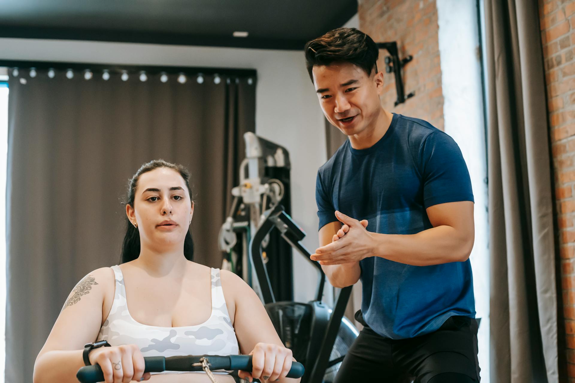 A personal trainer assists a woman in effective indoor rowing workout for peak fitness.