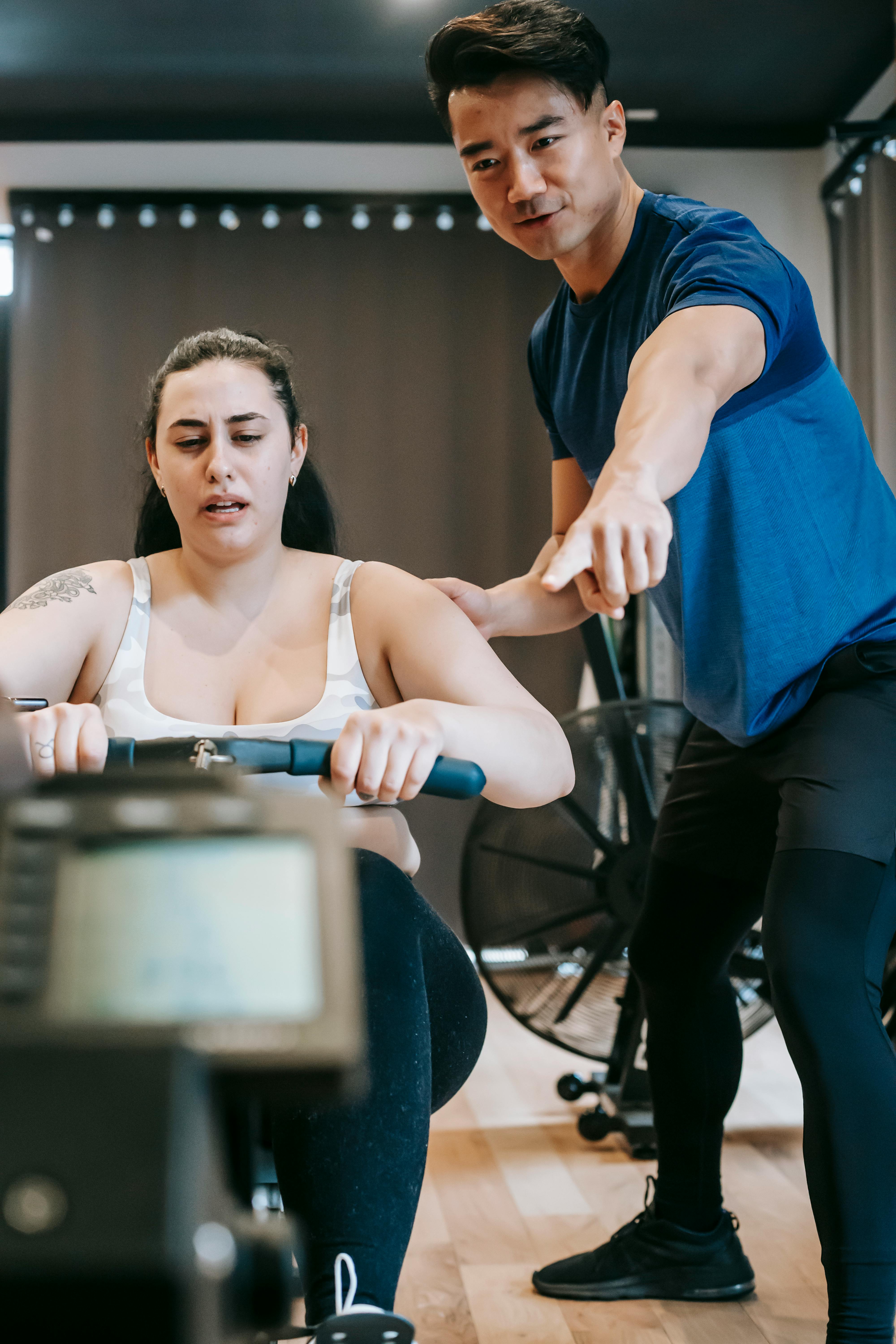 supportive ethnic trainer helping woman training on machine