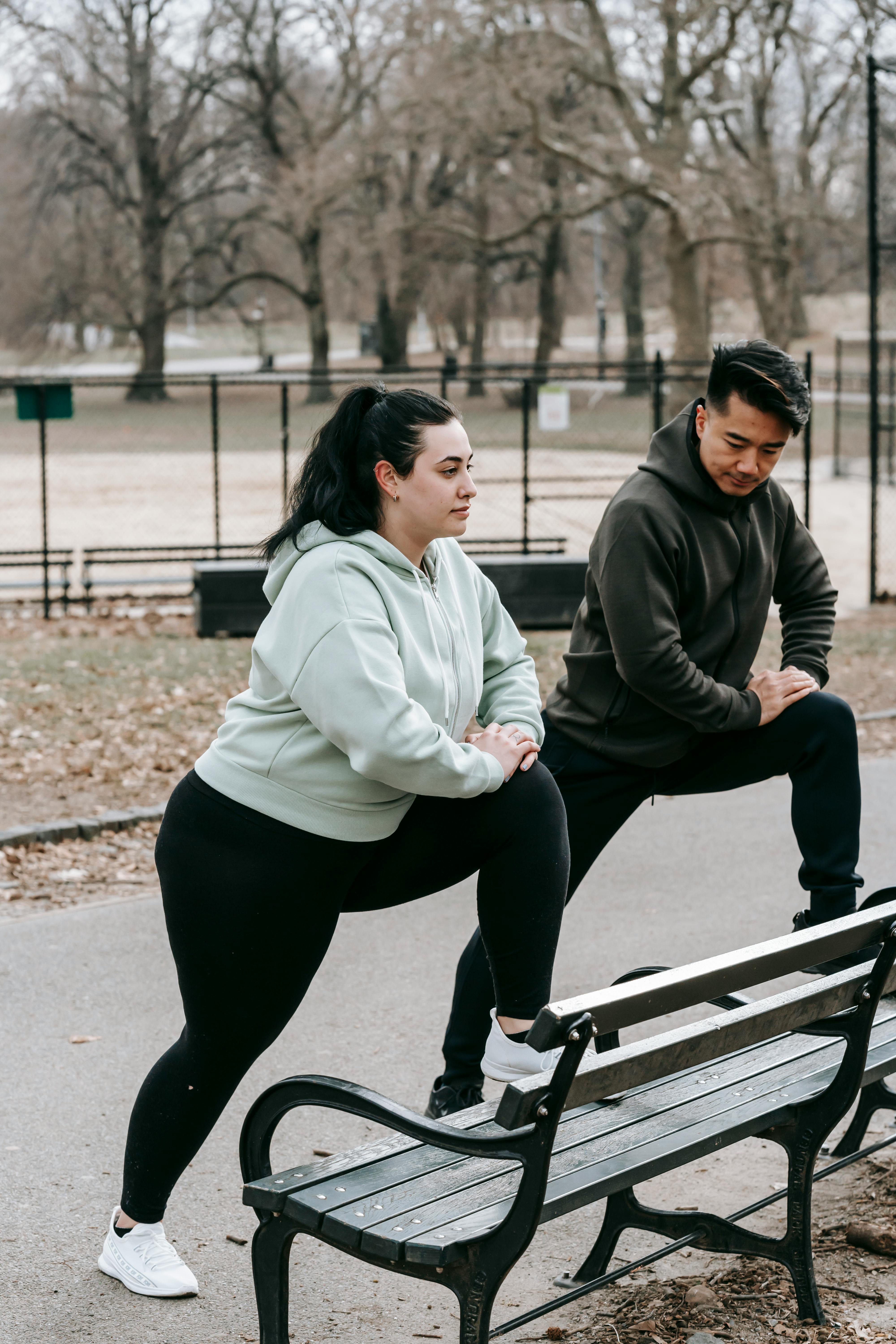 young obese female with ethnic male instructor exercising together in park