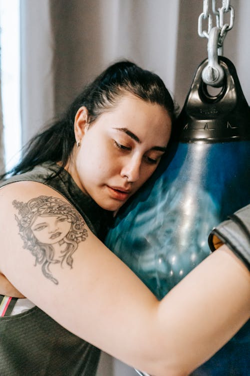 Tired young lady leaning on punching bag after boxing training