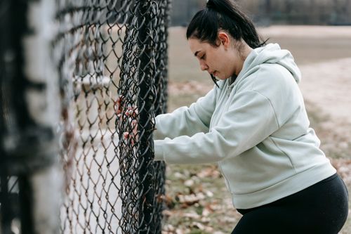 Free Side view of calm overweight female in sportswear standing near metal fence in park in daytime Stock Photo