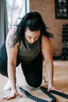 Focused plus sized female in sportswear exercising with battling ropes in equipped sports center