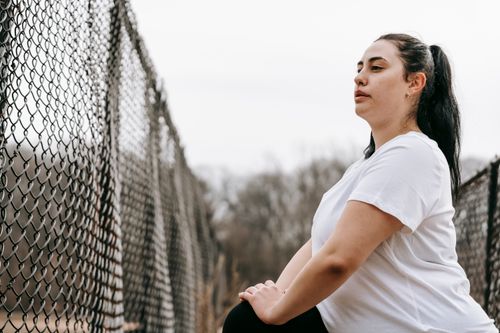 Free Side view concentrated plus sized sportswoman in white t shirt stretching legs near net fence in autumn countryside Stock Photo
