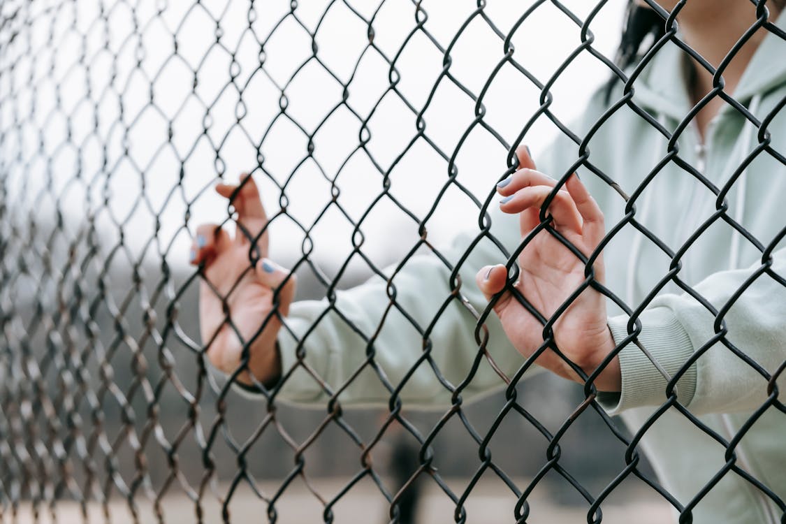 Free Crop unrecognizable woman touching net fence on street Stock Photo