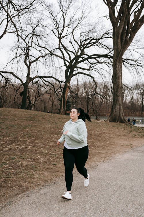 Full body motivated plus sized female in gray hoodie running in autumn park