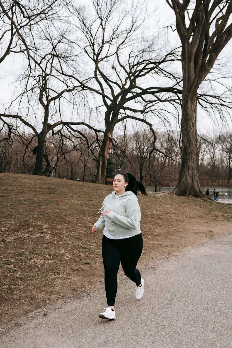 Plump Sportswoman Jogging In Leafless Park