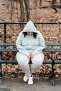 Full body sad plus sized brunette in hoodie sitting on bench in autumn park and looking down