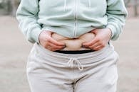 Crop anonymous plus sized female in casual hoodie touching and showing fat on belly while standing in park