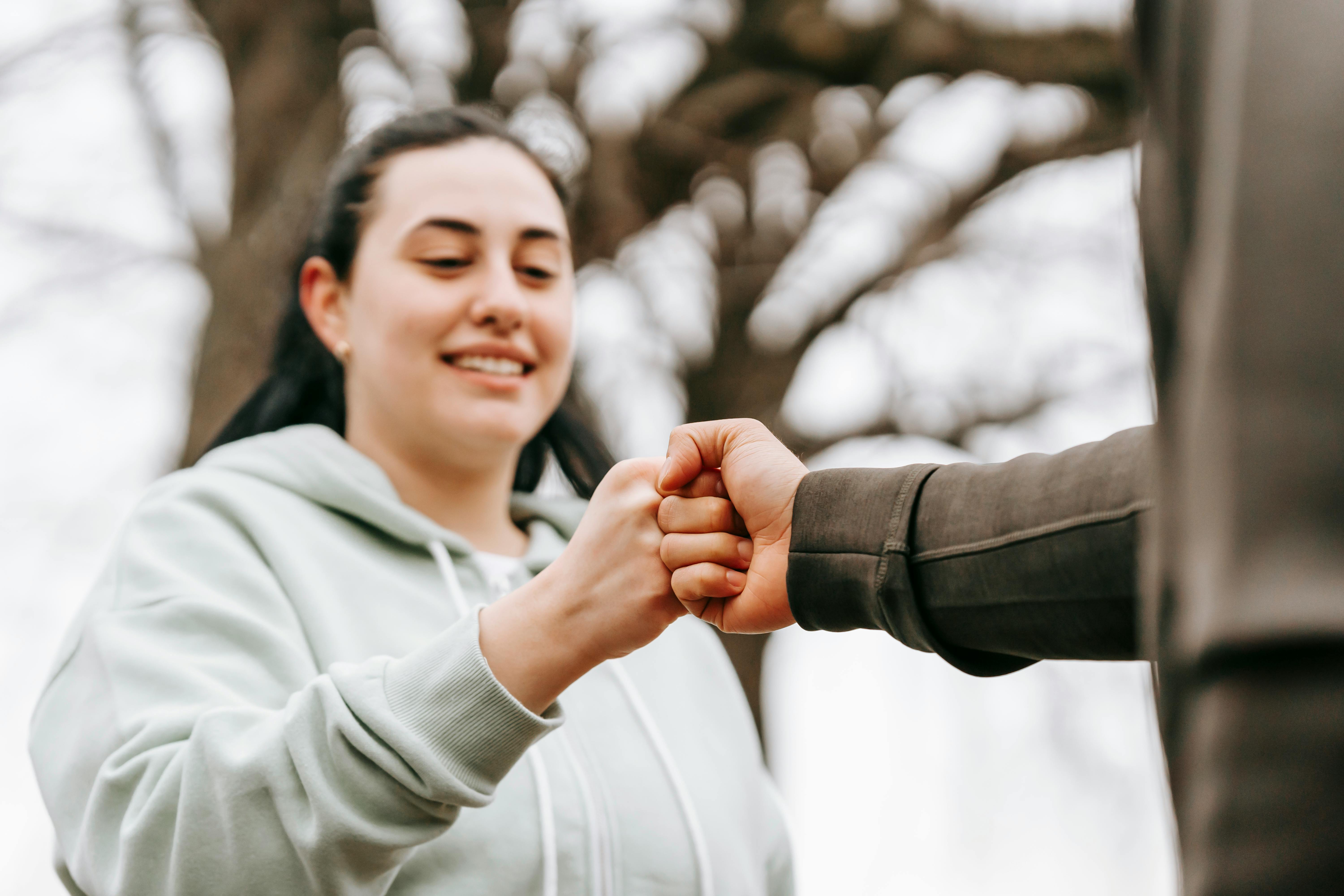 smiling woman bumping fists with friend in autumn park