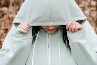 Crop unhappy female covering lowered head with hood in autumn forest in daylight