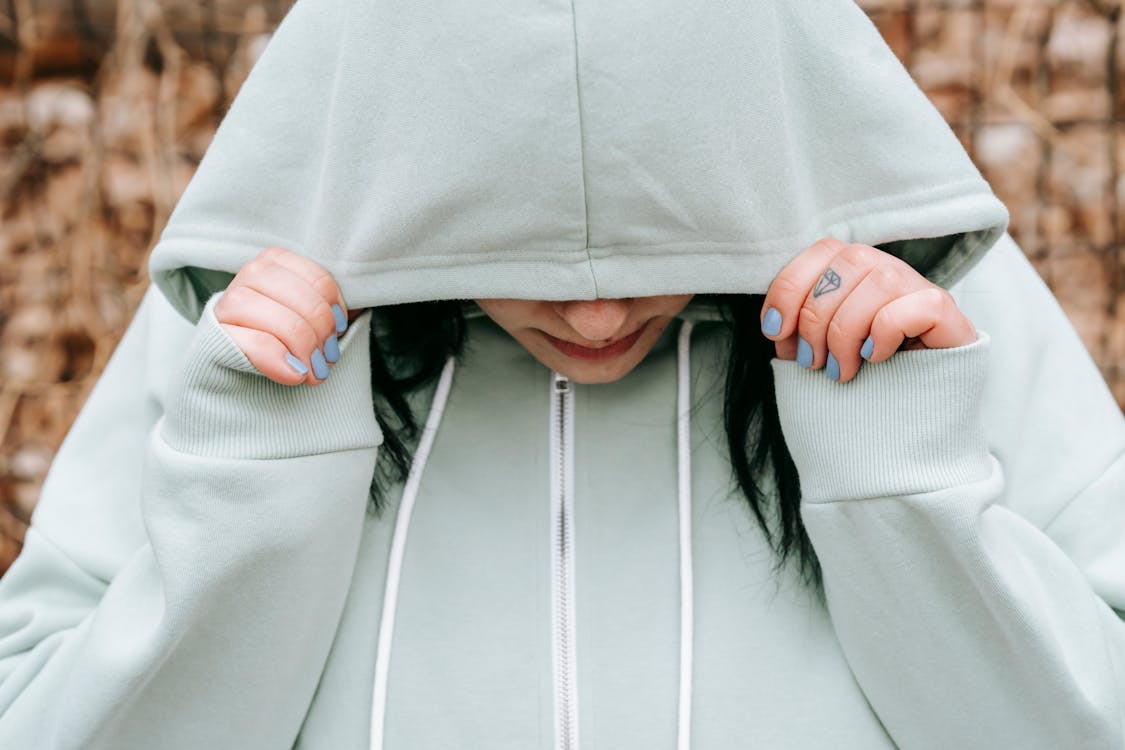Free Crop unhappy female covering lowered head with hood in autumn forest in daylight Stock Photo