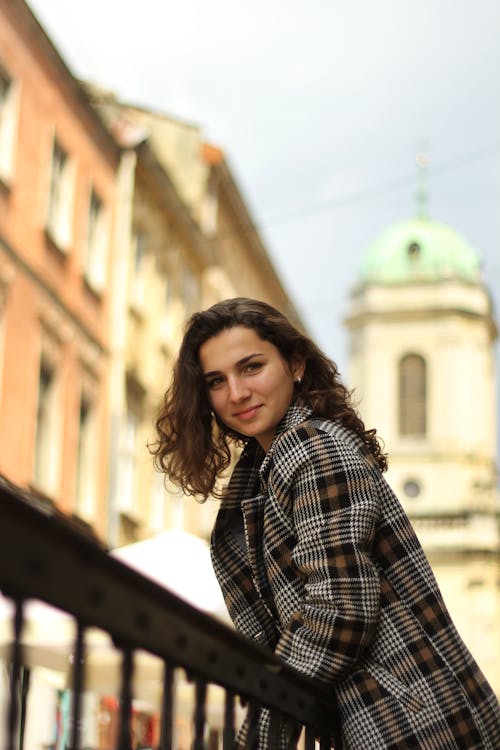 A Woman in Plaid Coat Smiling while Standing Near the Metal Railing