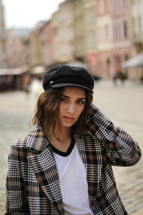 A Woman in Plaid Coat and Black Cap Standing on the Street