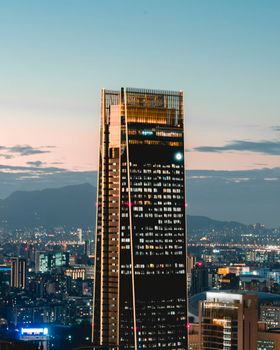 Modern town with illuminated multistory skyscraper near buildings under bright sky in evening