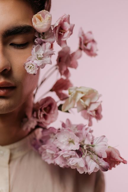 Close-up portrait of an Asian man with elegant pink flowers, set against a pastel background for a soft, artistic feel.