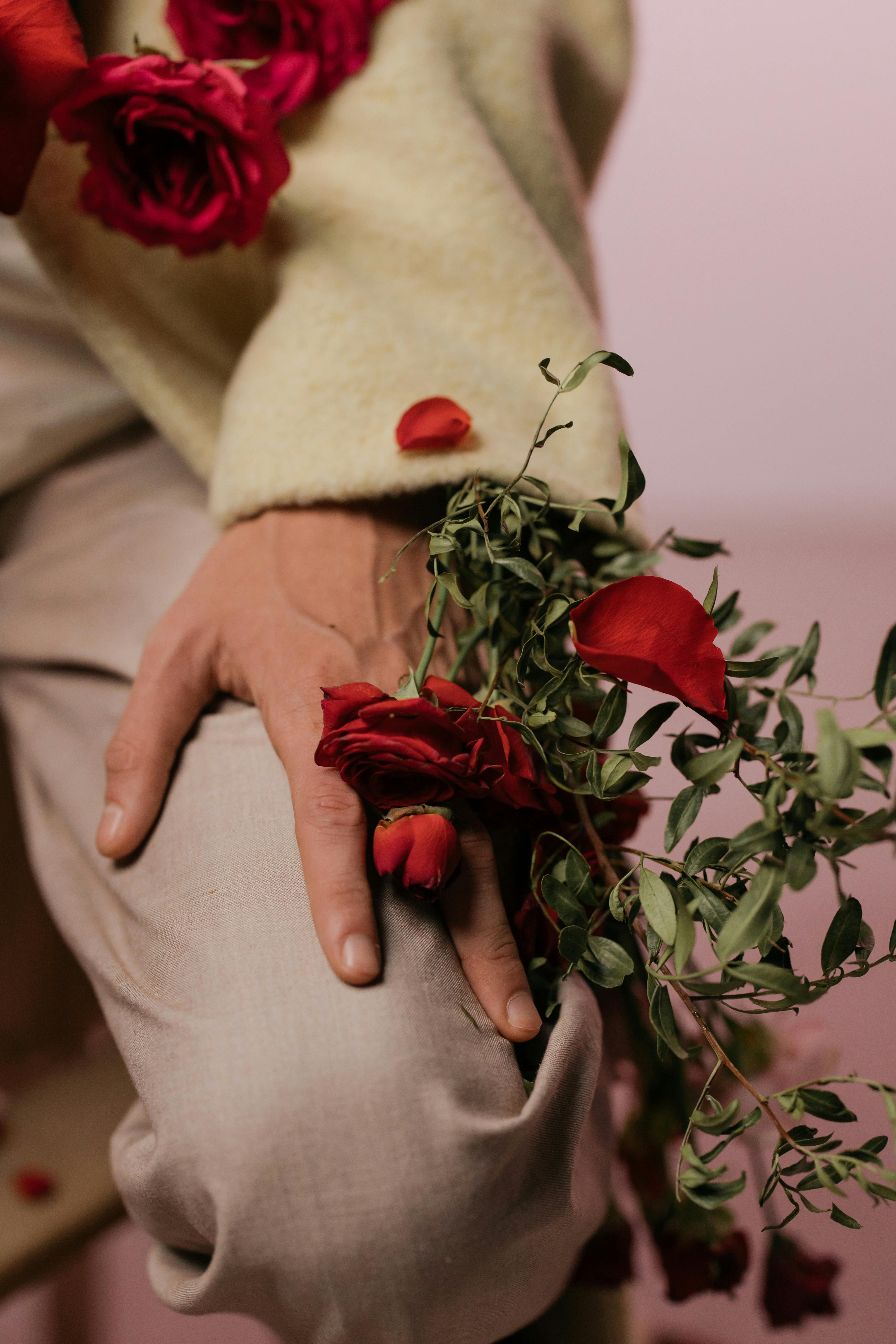 A man's hand with delicate red roses and lush greenery in an artistic composition.
