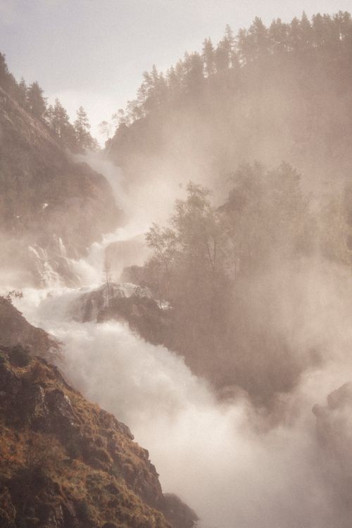 Free A scenic view of a cascading waterfall enveloped in mist within a foggy forest, creating a serene nature scene. Stock Photo