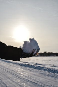 A hand holding a snowball against a winter sunset backdrop in Estonia.