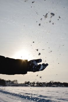 A person in winter gloves throws snow into the sunlit sky, capturing the essence of a cold day.