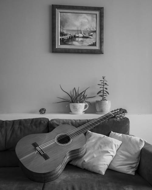 Grayscale Photo of an Acoustic Guitar on the Sofa
