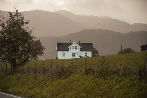 Free Scenic rural house in a lush field with majestic mountains in the background. Stock Photo