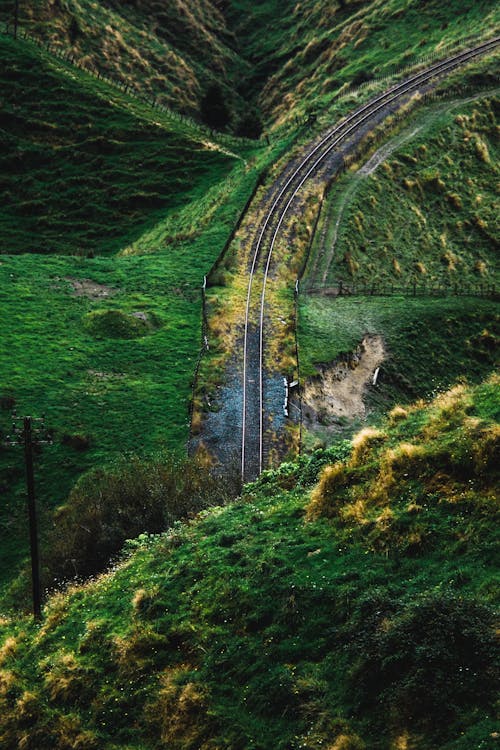High angle of railway road surrounded with green grassy meadows on hills in daylight